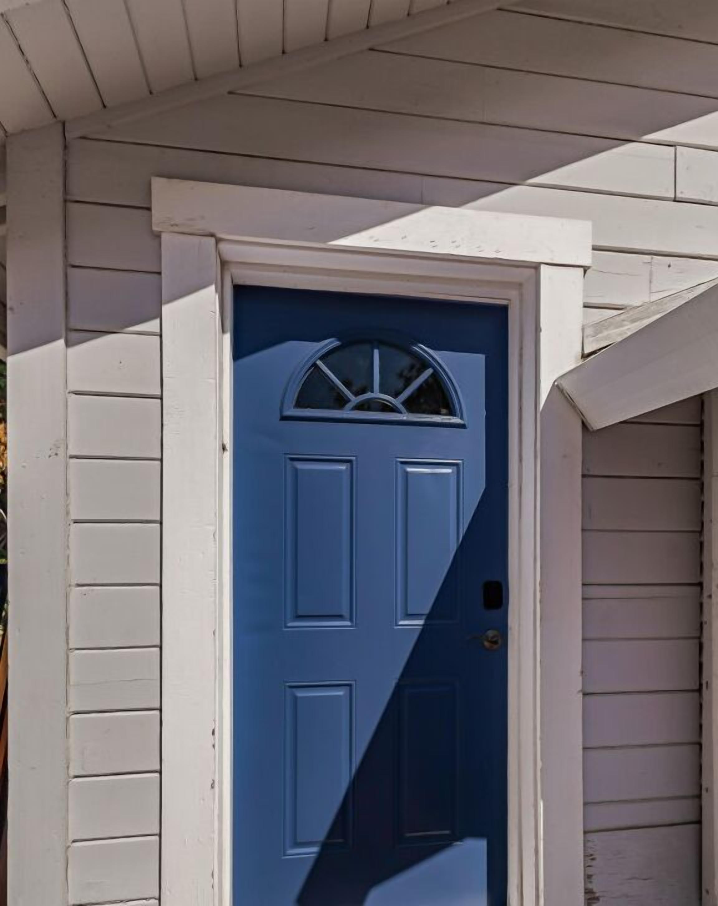A white exterior wall with a blue door featuring a semi-circular window above it.