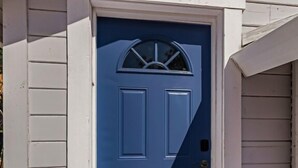 A white exterior wall with a blue door featuring a semi-circular window above it. - Charming Avenue Guest House (Chico)