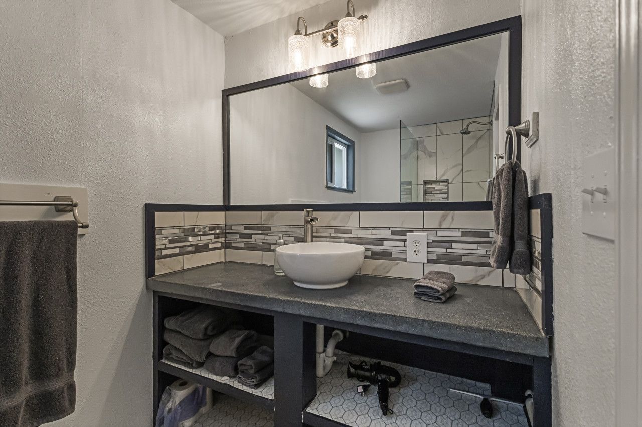 A bathroom with a large mirror, a white sink, a towel rack, and a towel on the wall.