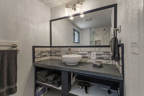 A bathroom with a large mirror, a white sink, a towel rack, and a towel on the wall. - Charming Avenue Guest House (Chico)