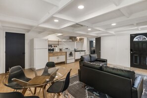 Une cuisine moderne avec des meubles blancs, un coin repas doté d’une table en verre et de chaises noires, ainsi qu’un canapé en cuir noir.