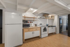 A modern kitchen with white cabinetry, a built-in microwave, oven, and a refrigerator. There are wooden shelves above the counter and a skylight above. - Charming Avenue Guest House (Chico)