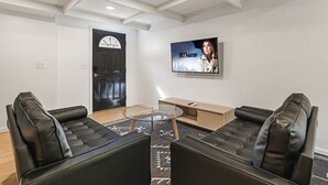 A modern living room with two black leather sofas, a glass coffee table, and a TV mounted on the wall. - Charming Avenue Guest House (Chico)