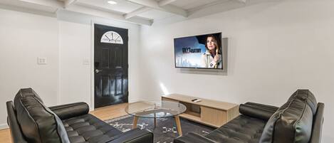 Una sala de estar moderna con dos sofás de cuero negro, una mesa de centro de vidrio y un televisor montado en la pared.