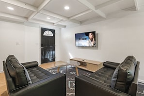 A modern living room with two black leather sofas, a glass coffee table, and a TV mounted on the wall. - Charming Avenue Guest House (Chico)