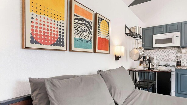 A modern hotel room with a bed, a kitchenette, and three abstract wall art pieces. - Chic Guesthouse Near Downtown | Stylish, Private & Cozy (Chico)