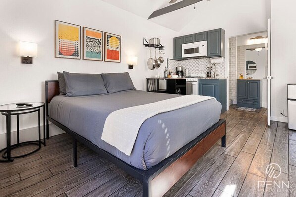 A modern bedroom with a large bed, bedside tables, and a small kitchen area with cabinets and a microwave.