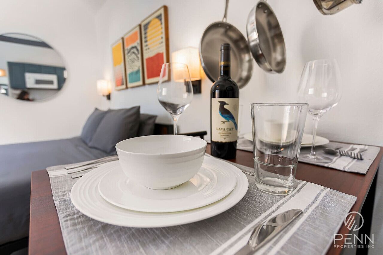 A dining table set with a white bowl, plates, and cutlery, a bottle of wine, and two glasses of water.