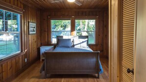 Een slaapkamer met houten lambrisering, een bed, een nachtkastje en een plafondventilator.