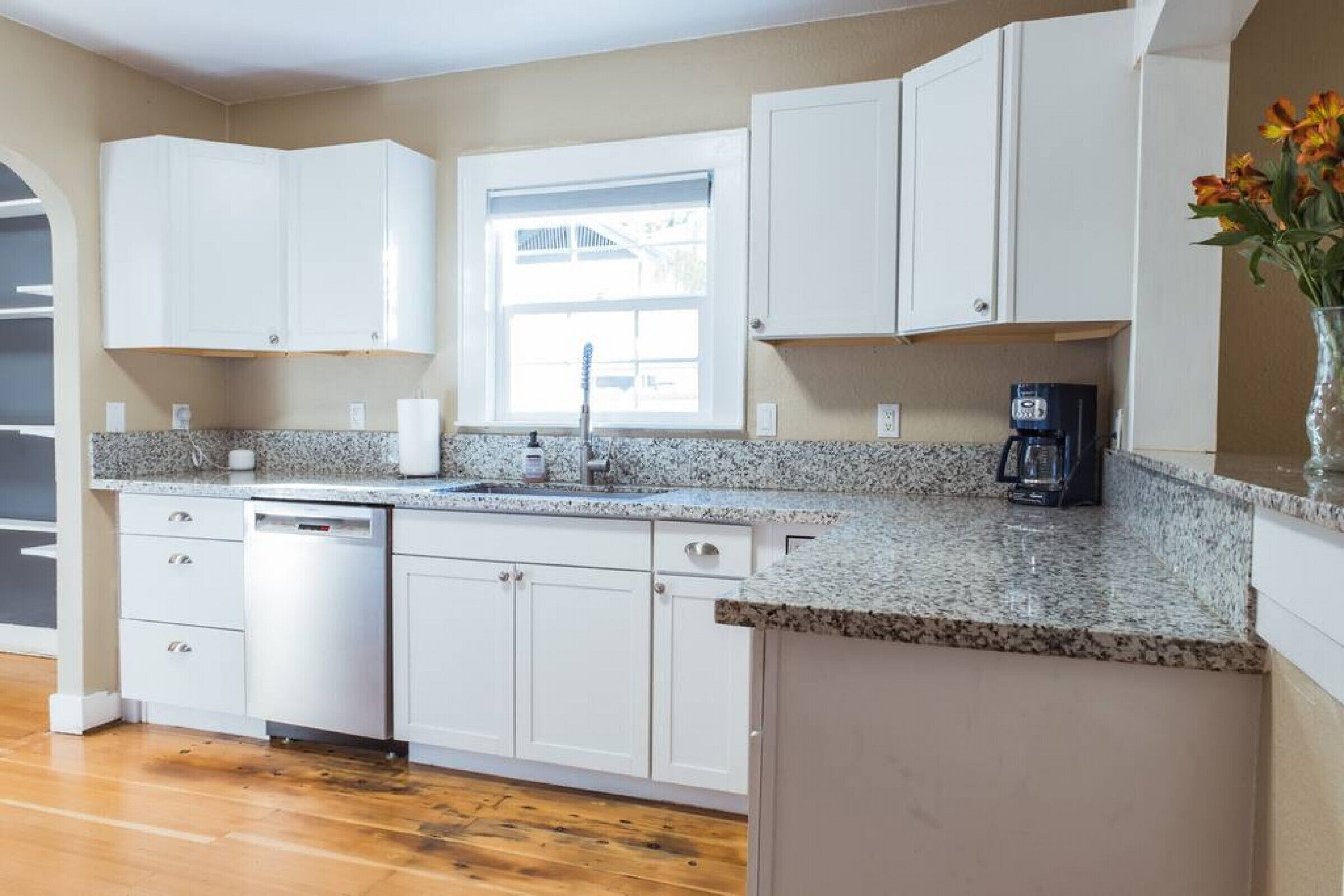 A kitchen with white cabinets, a granite countertop, a dishwasher, and a coffee maker.