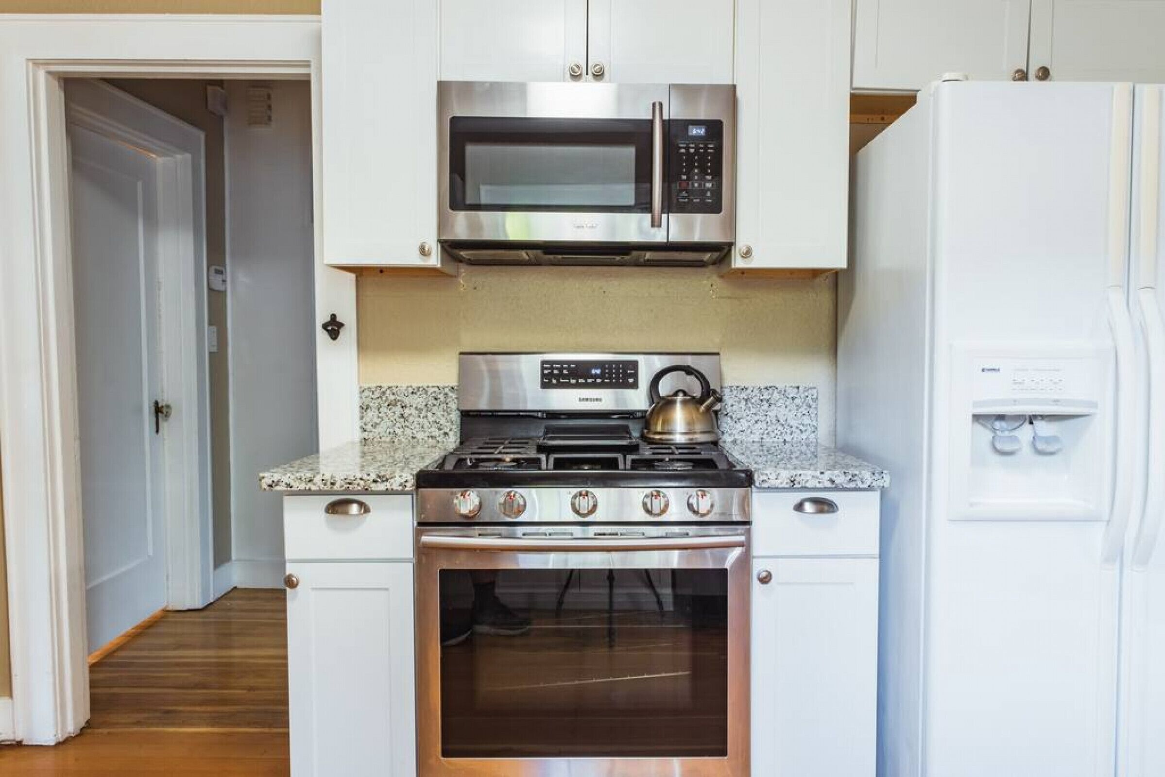 A kitchen with white cabinets, a stainless steel microwave, a gas stove, and a built-in oven.