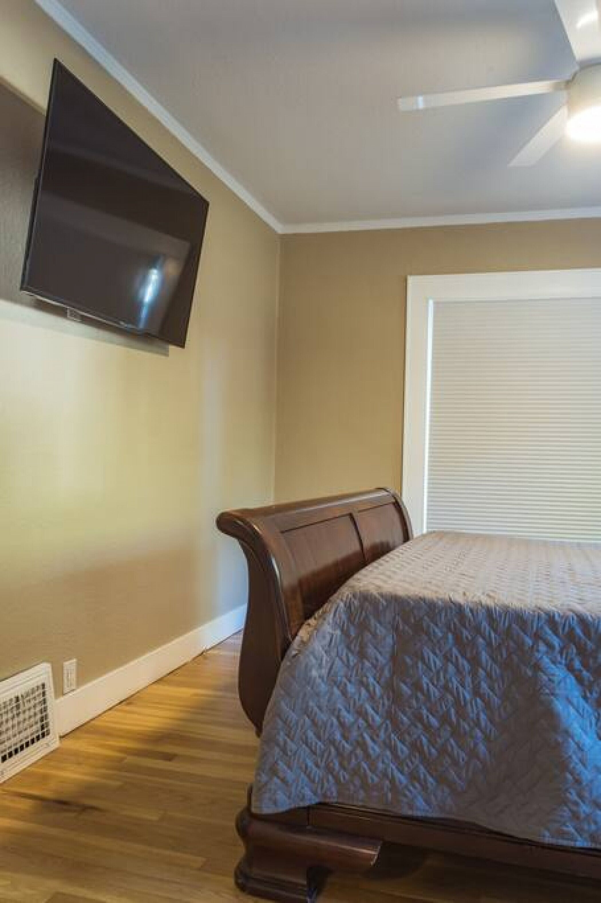 A bedroom with a bed, a TV mounted on the wall, and a ceiling fan.