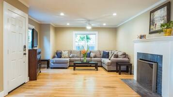 A living room with a sectional sofa, a coffee table, a fireplace, and a television.