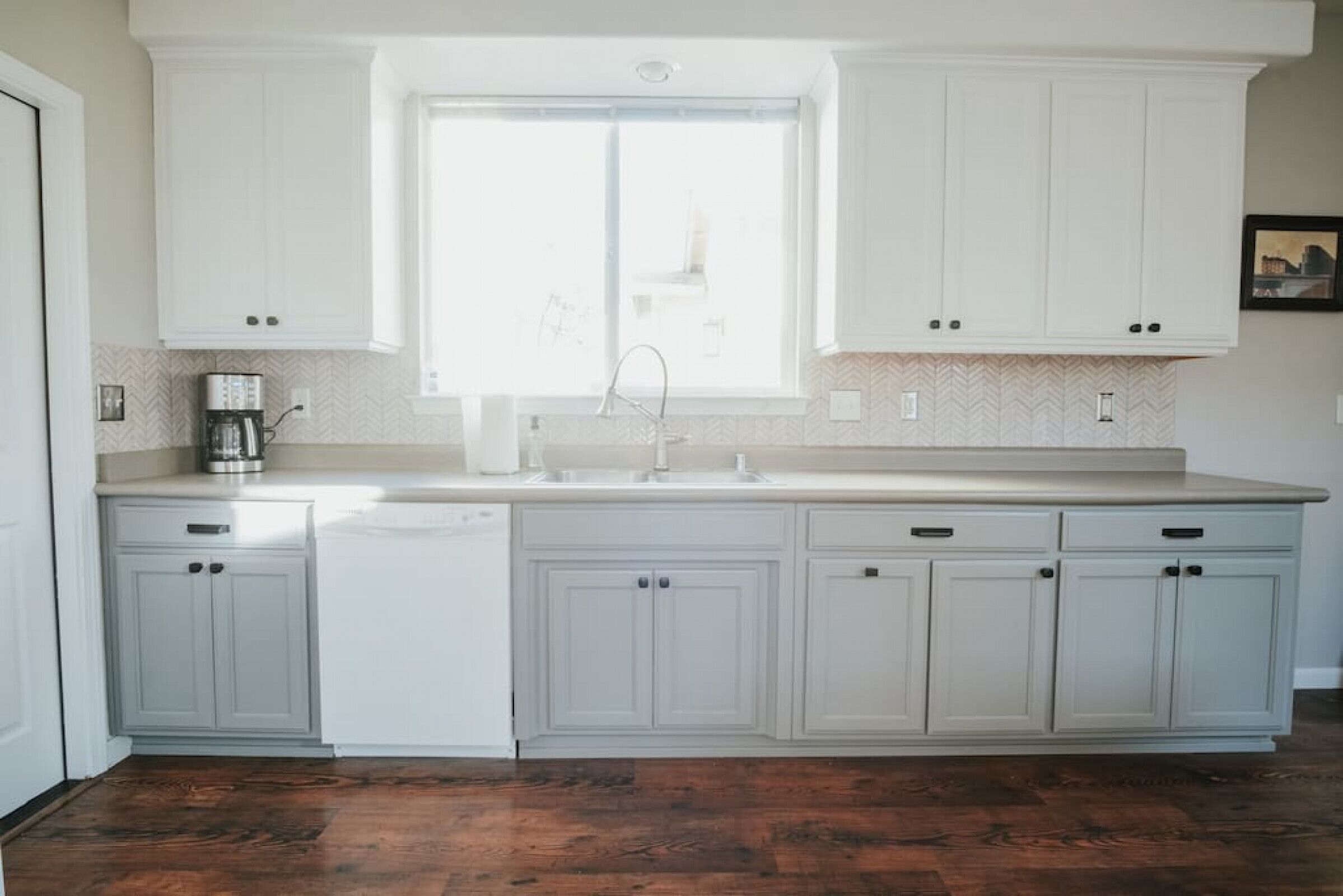A kitchen with white cabinets, a window, and a dishwasher.