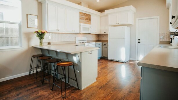 A modern kitchen with white cabinetry, a central island with stools, and a large refrigerator.