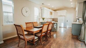 A spacious kitchen with white cabinets, a wooden dining table with chairs, and a clock on the wall.