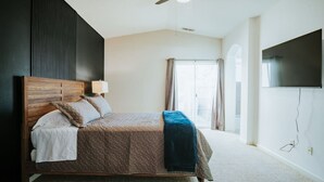 A bedroom with a bed, a ceiling fan, a TV, and a window with curtains.