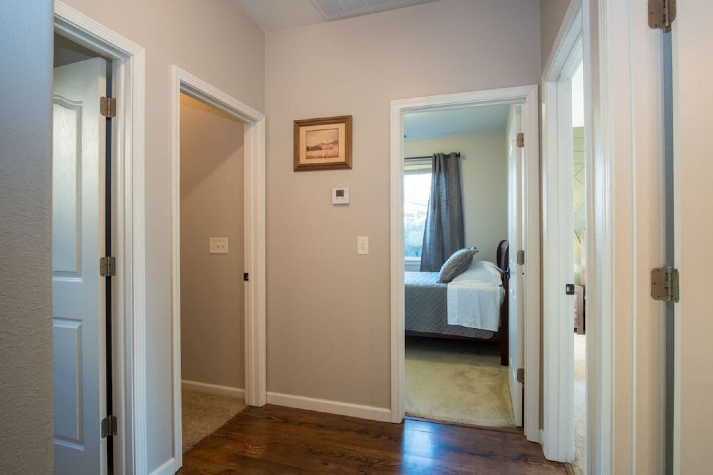 Un pasillo con piso de madera, una puerta a la izquierda y una habitación visible a través de una puerta abierta a la derecha.