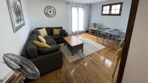 A modern living room with a sofa, coffee table, and a dining area with chairs and a TV. - Gite Jeanroy a Cheerful 2 Bedroom Rural Gite (Saint-Martial-Viveyrol)