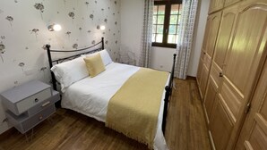 A bedroom with a bed, a nightstand, a wardrobe, and a window with curtains. - Gite Jeanroy a Cheerful 2 Bedroom Rural Gite (Saint-Martial-Viveyrol)