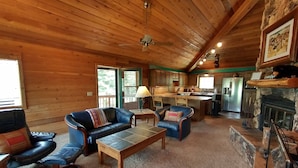 A cozy cabin interior with a wooden ceiling, a fireplace, a dining area, and a seating area with leather sofas. - Mountain Cabin with Multi-level Decks, Views, Hot Tub, Family Memories Made Here (Angel Fire)