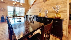 Un interior de madera con una gran mesa de comedor, sillas, una araña y jarrones decorativos sobre un aparador.