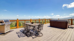 Una terraza de madera con una mesa, sillas, una parrilla y un jacuzzi.