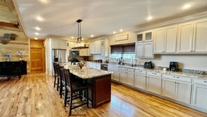 Una cocina amplia con una isla grande, suelo de madera, armarios blancos y horno empotrado.