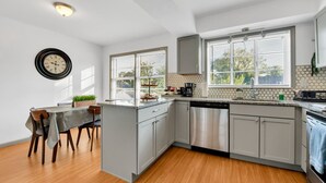 Une cuisine moderne avec des meubles gris, un lave-vaisselle et un coin repas comprenant une table et des chaises.