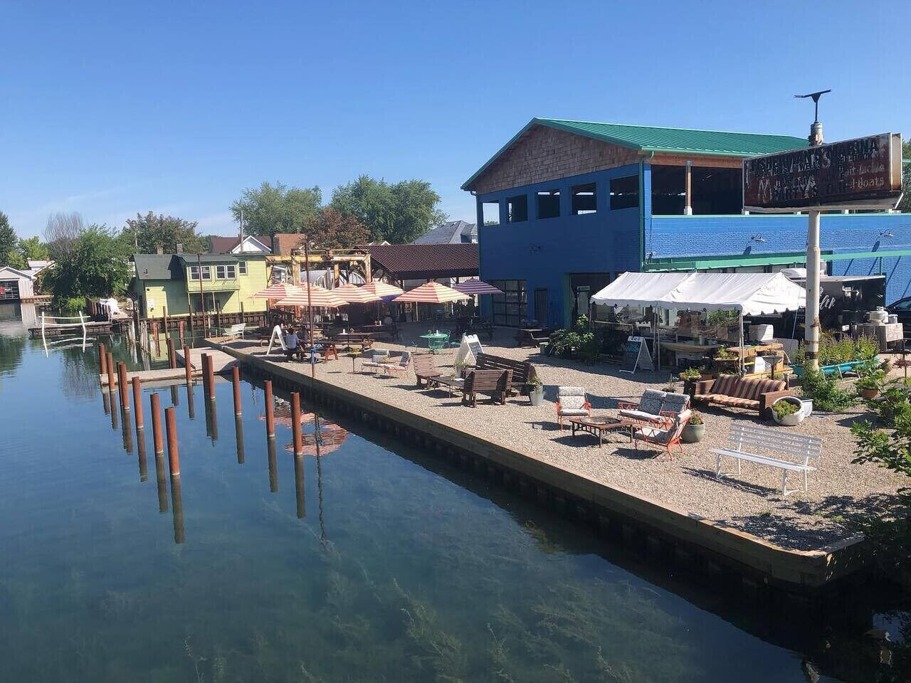 Una propiedad frente al agua con un muelle que se adentra en el agua, asientos al aire libre y un edificio con techo verde.