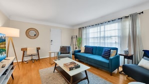 Un salon moderne avec un canapé bleu, une table basse blanche et un bureau avec une lampe.