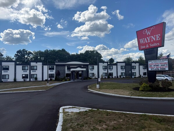 A Wayne Inn & Suites with a modern building facade, a clear sky, and a parking area.
