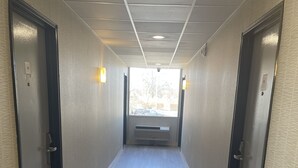 Un couloir avec deux portes de chaque côté, un plafond doté d’un éclairage encastré et une fenêtre au bout.