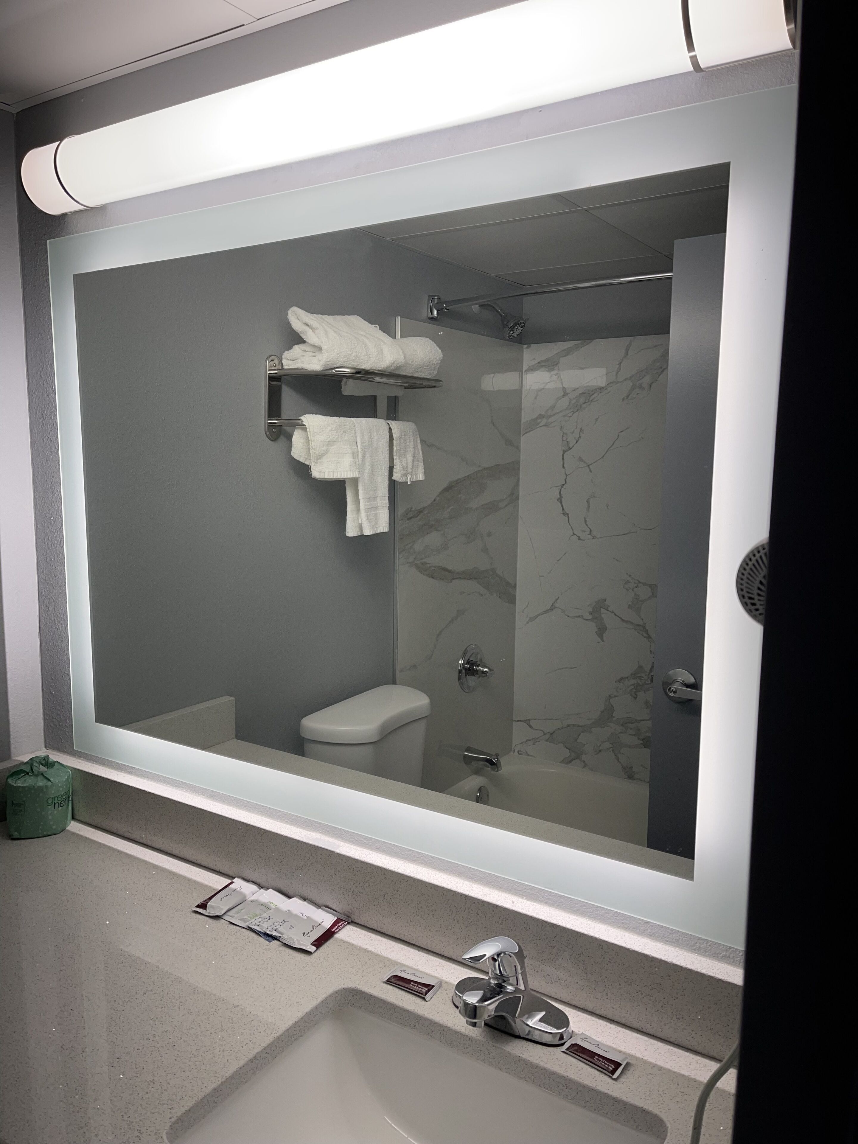 A modern bathroom with a large mirror, a toilet, a shower, and a sink.