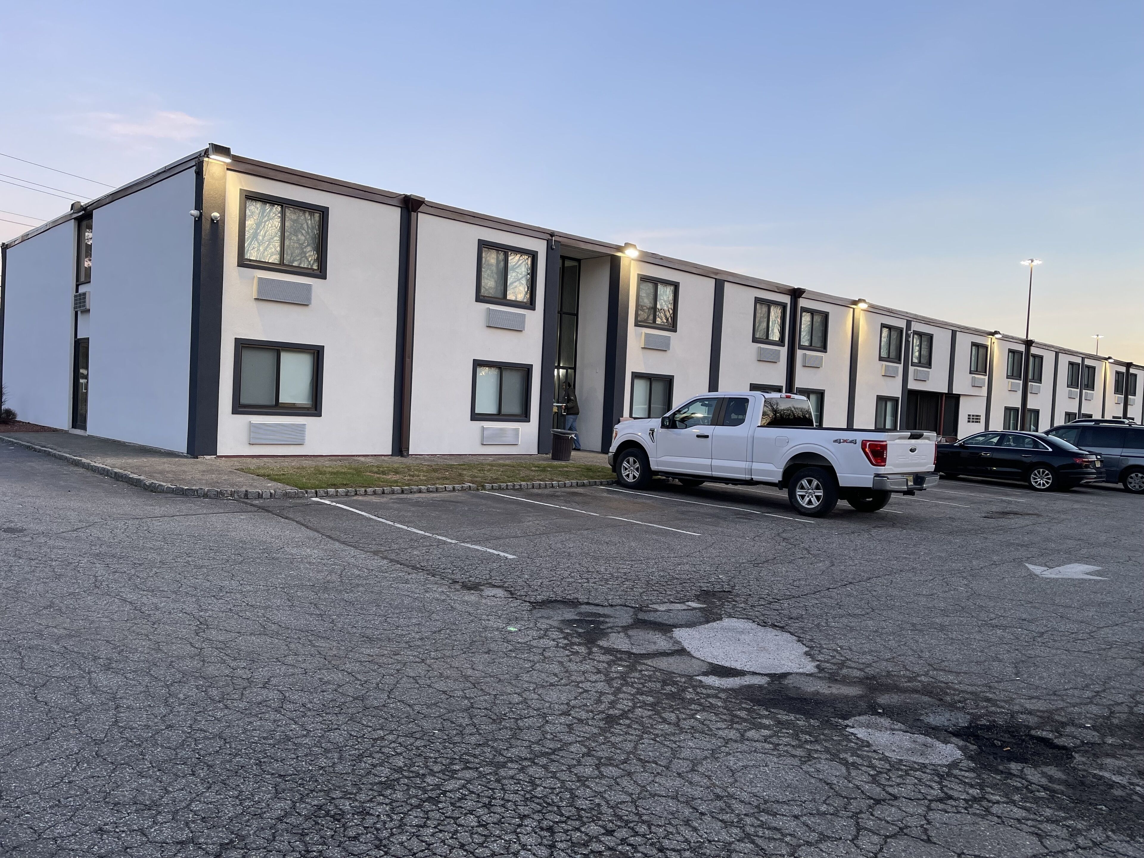Een rij moderne, twee verdiepingen tellende gebouwen met een parkeerplaats ervoor.
