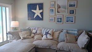 Een woonkamer met een groot kunstwerk van een zeester, een bank met kussens met strepen en zeestermotieven, en een bijzettafeltje met een lamp.
