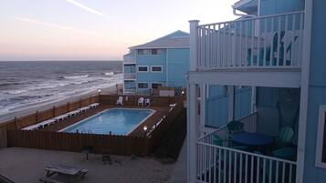 A beachfront property with a pool, outdoor seating, and a balcony with chairs.
