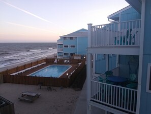 A beachfront property with a pool, outdoor seating, and a balcony with chairs.