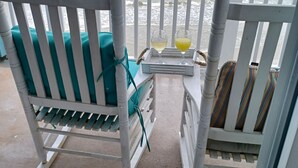 Een balkon aan het strand met een witte schommelstoel en een tafeltje met twee glazen.