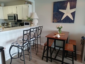 A kitchen with white cabinets, a microwave, and a tablet on the counter. There are two chairs with star patterns and a table with a vase of flowers.