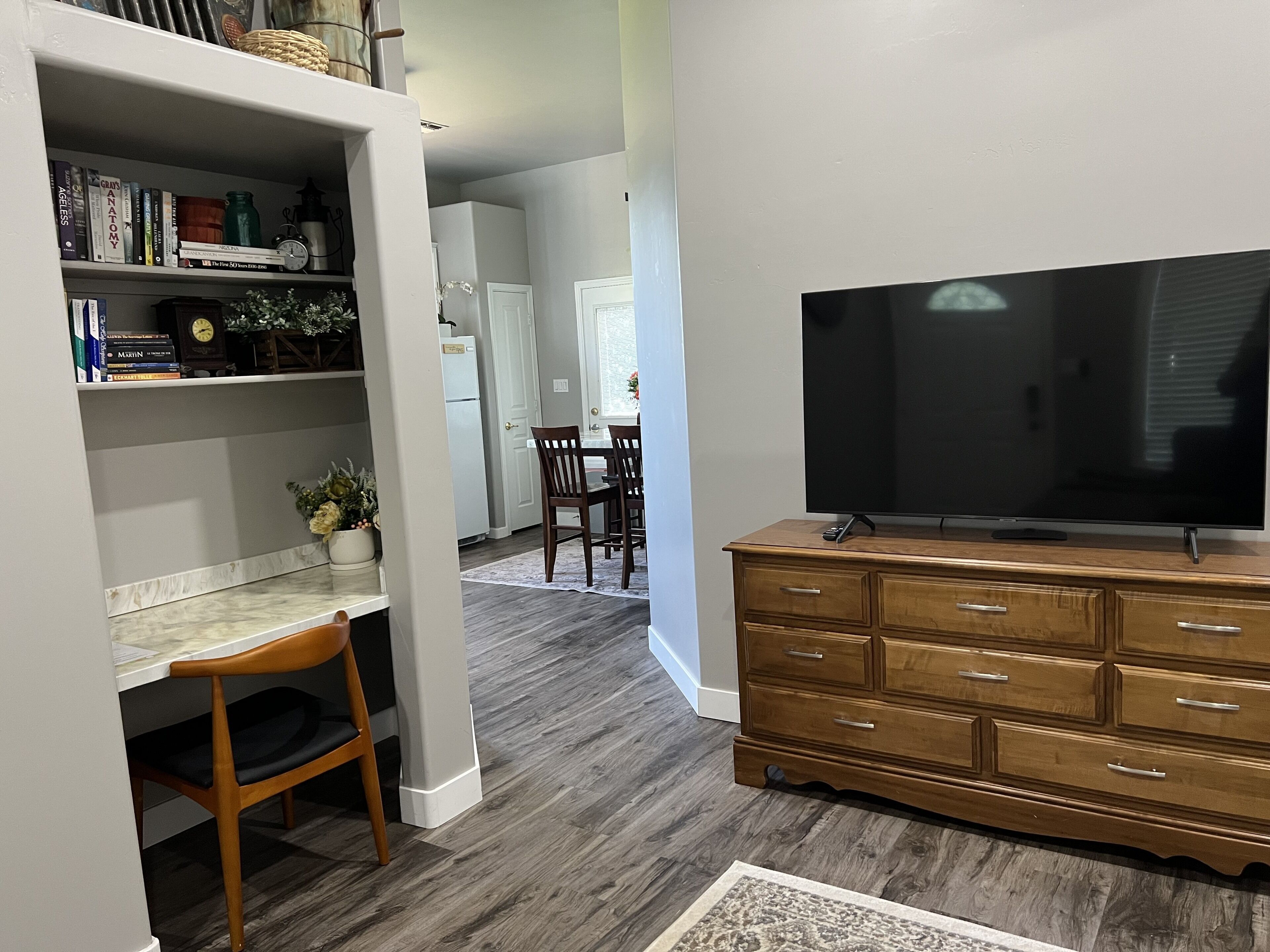 A modern living room with a flat-screen TV, wooden dresser, and a dining area with chairs and a table.