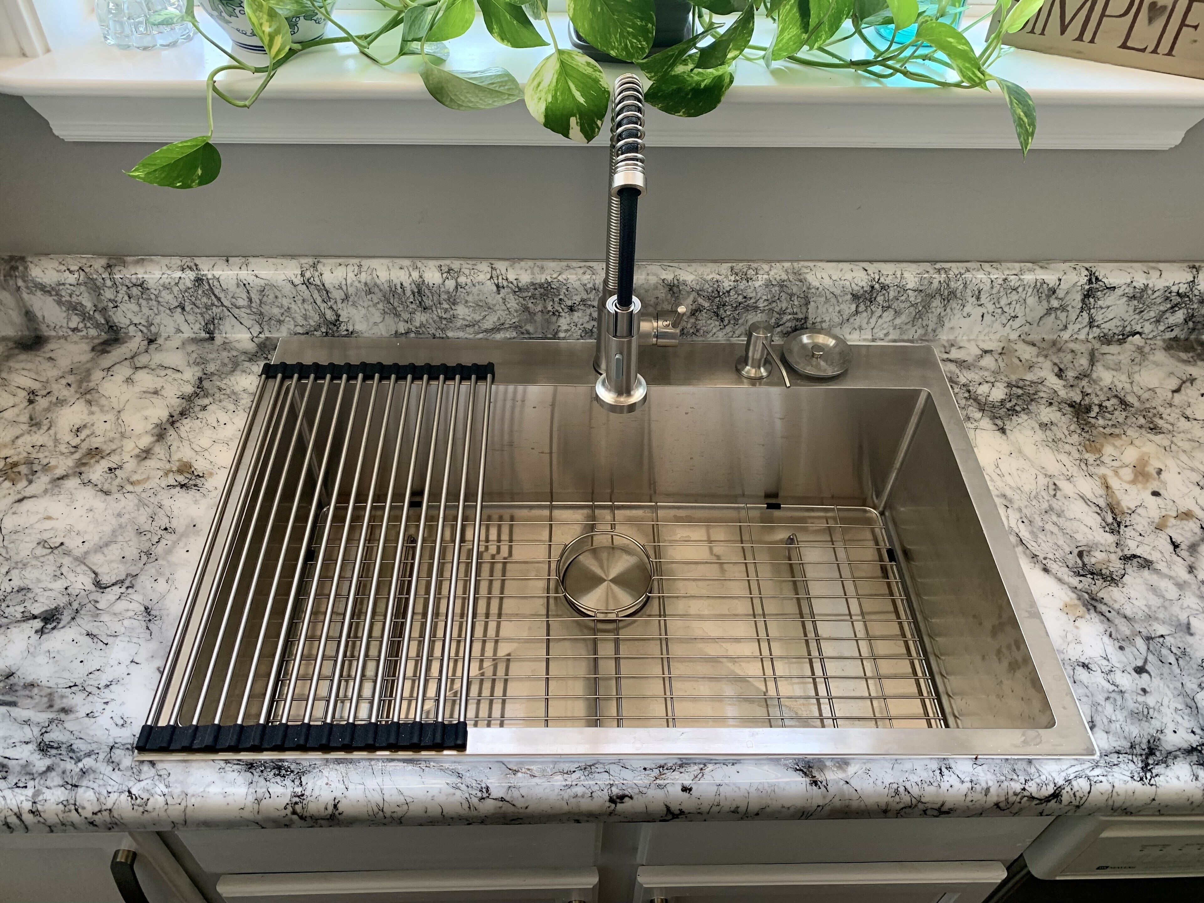 A kitchen sink with a stainless steel faucet, a grid strainer, and a marble countertop.