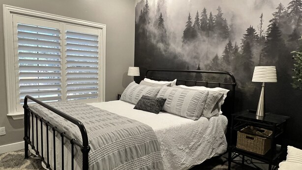 A bedroom with a bed, a nightstand, a lamp, a window with blinds, and a forest mural on the wall. - Country Living in the City (Mesa)