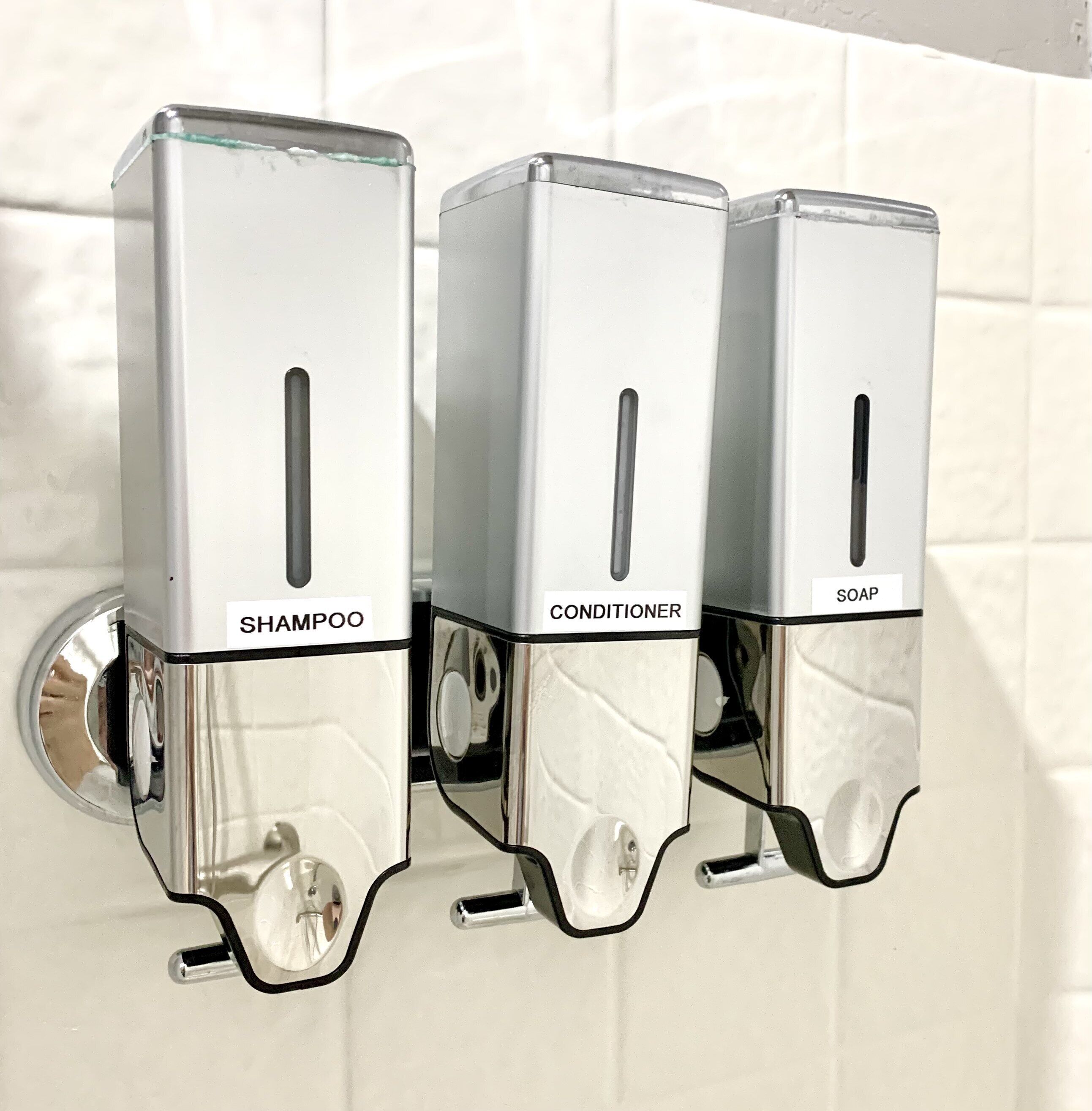Three wall-mounted dispensers labeled for shampoo, conditioner, and soap.
