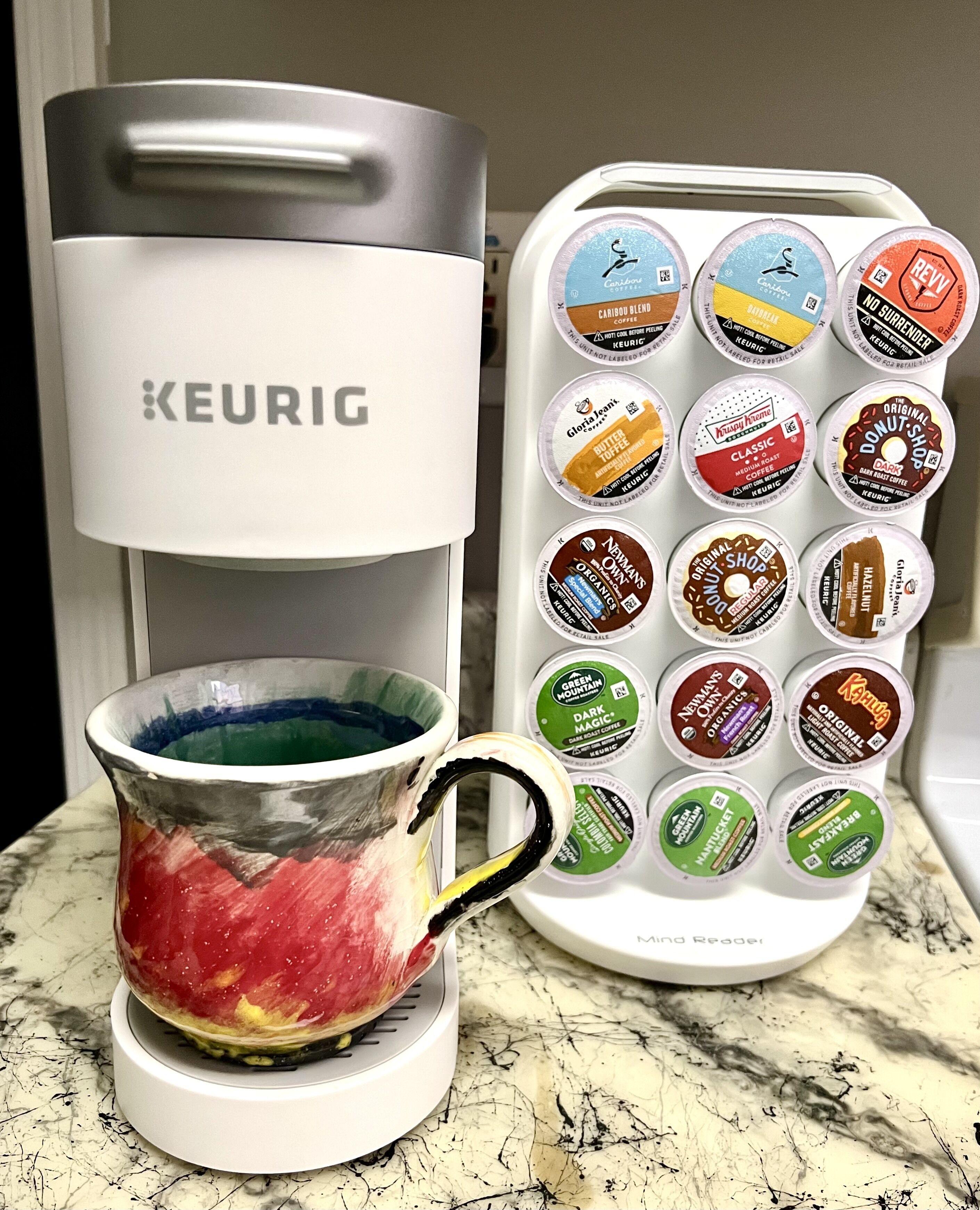 Une machine à café Keurig avec une tasse remplie de café et un assortiment de dosettes de café.