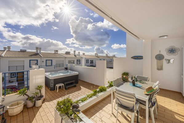 A rooftop terrace with a hot tub, outdoor seating, potted plants, and a view of neighboring buildings.
