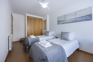 A hotel room with two beds, a ceiling fan, a radiator, and a painting on the wall.