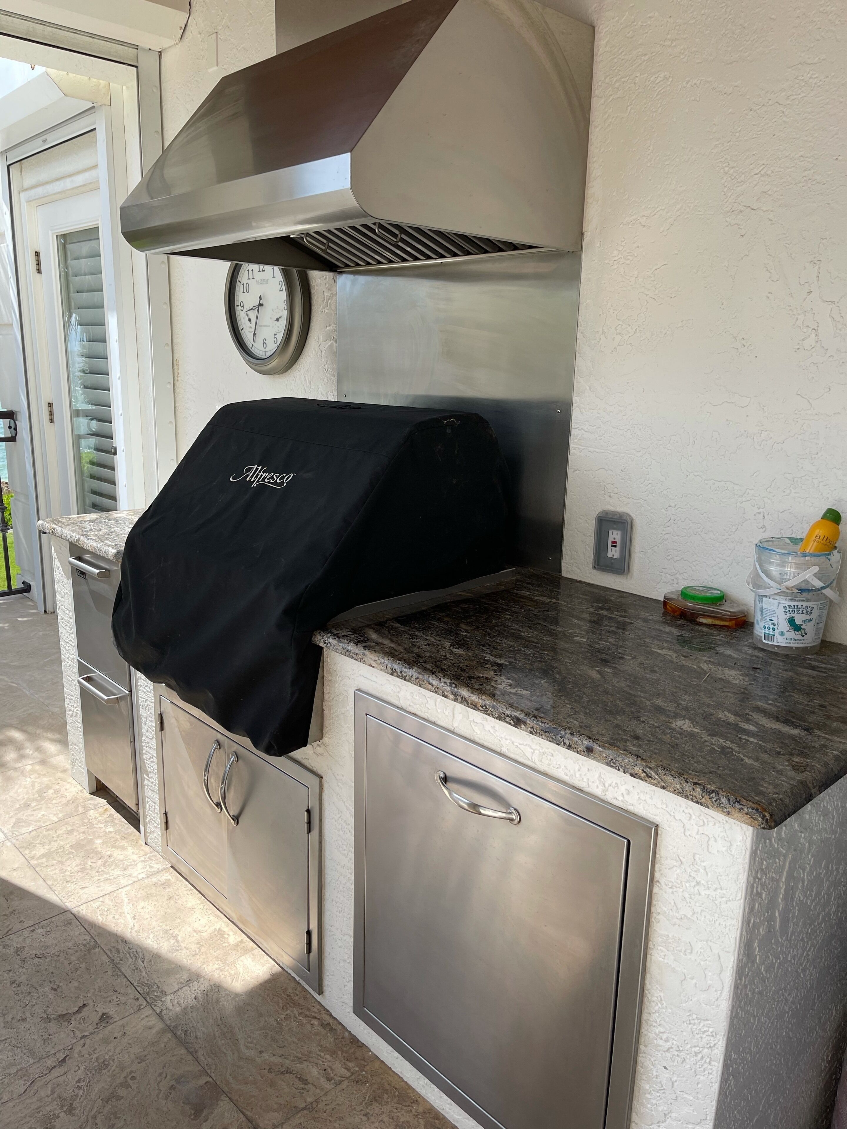 A kitchen with a built-in grill, stainless steel cabinets, and a clock on the wall.