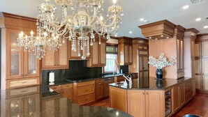 A spacious kitchen with wooden cabinets, a granite island, and a large chandelier.