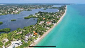 Vista aérea de una zona costera con edificios residenciales, una playa de arena y una extensa masa de agua.